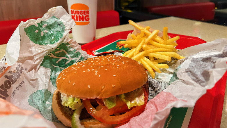 A Burger King Whopper and fries unwrapped on a red tray at a table in the restaurant, with a Burger King-branded drink cup visible