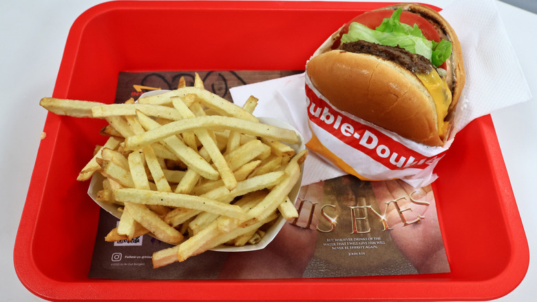 A red tray with a burger wrapped in In-N-Out branded paper and a side of fries