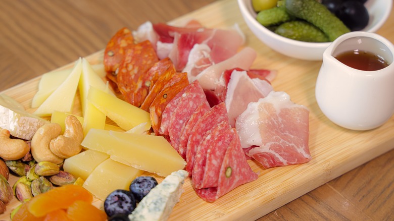 A charcuterie board with deli meats, cheese, and pickles