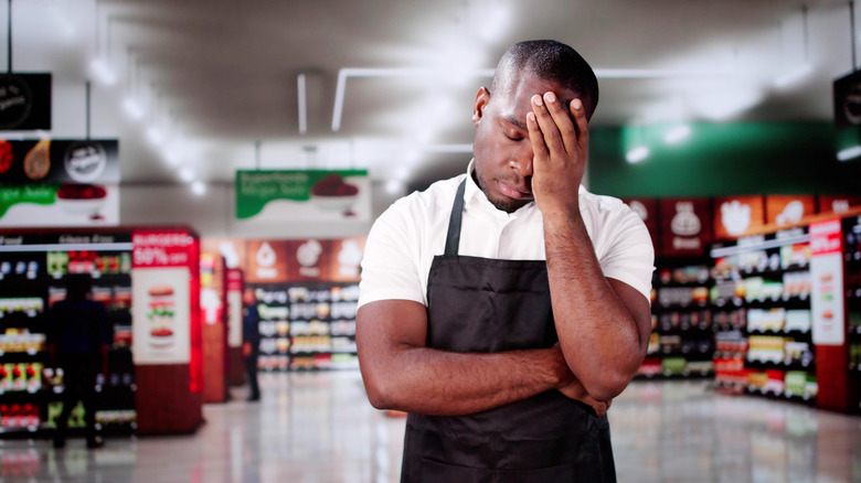 A supermarket employee holds his head in his hand in frustration.