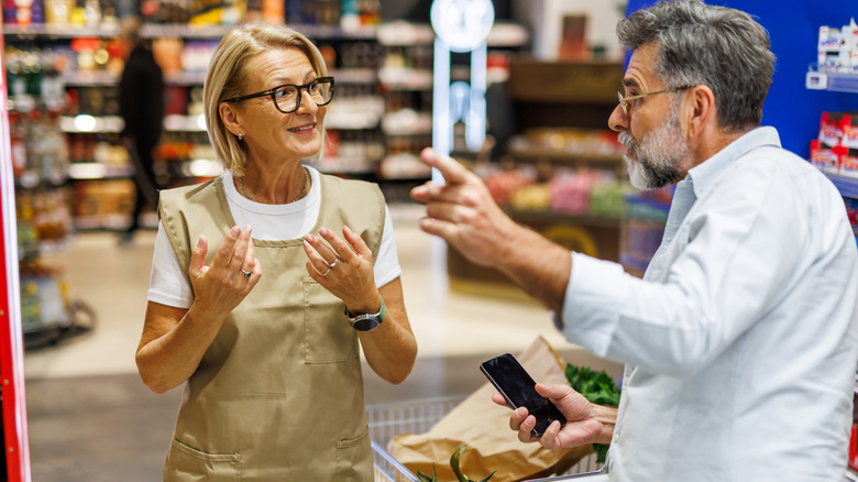 A man in a supermarket asks an employee for help.