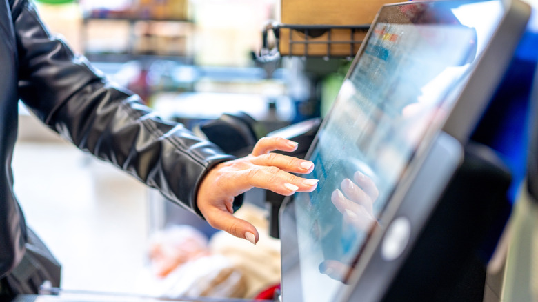 A hand presses a self-checkout monitor.