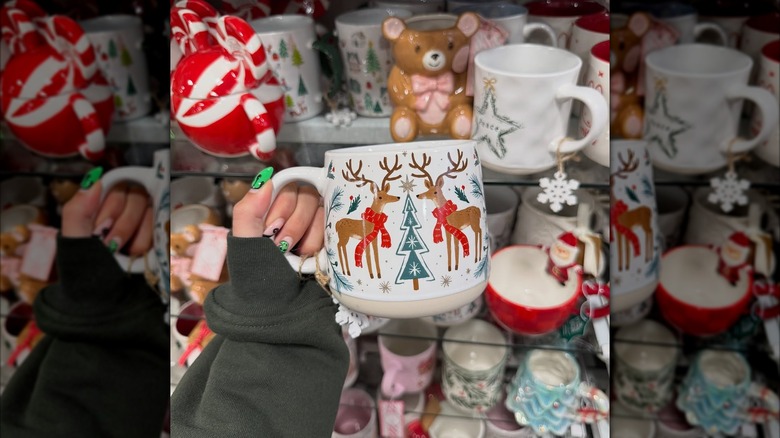 A hand holding a mug with reindeers and a tree in front of shelves of mugs