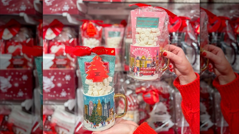 hands holding mugs in wrappers with marshmallows and hot chocolate mix