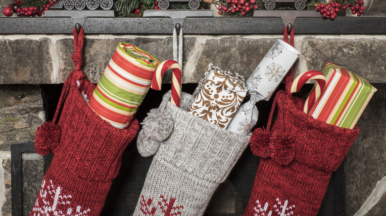 Presents stick out of red and gray knit stockings on a stone fireplace mantle.