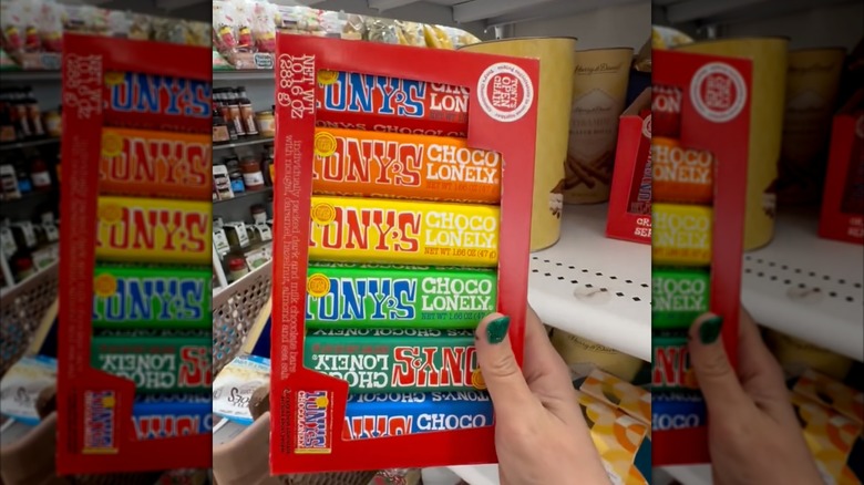 a hand holding a colorful box of Tony's Chocolonely chocolate bars