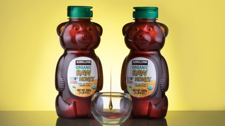 two Kirkland organic raw honey bottles with yellow background