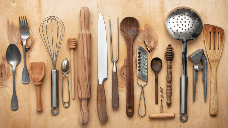 Variety of kitchen utensils such as knives, whisks, spoons, and more on wood surface