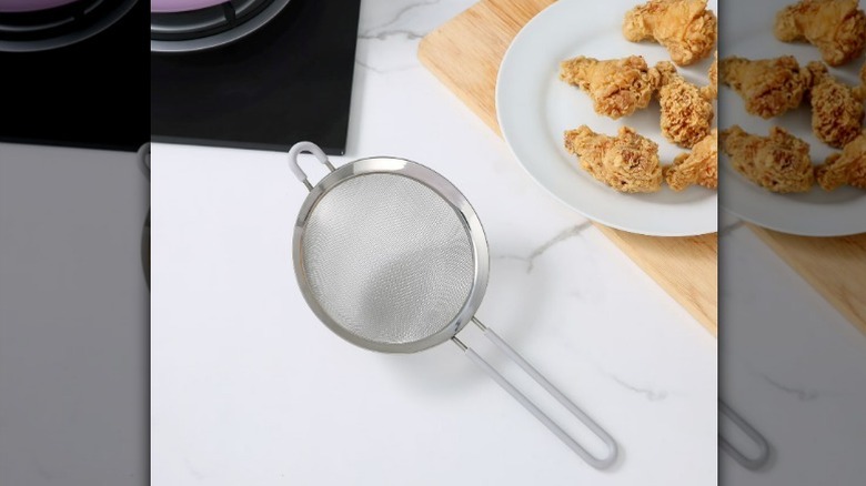 A metal fine mesh strainer by plate on a white marble countertop
