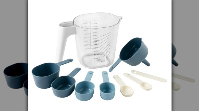 Stackable measurable set with large clear liquid measuring cup, smaller blue measuring cups, and cream measuring spoons on white background