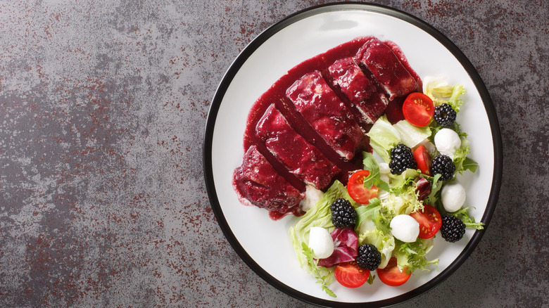 A plate of grilled chicken smothered in blackberry sauce with a blackberry salad on the side