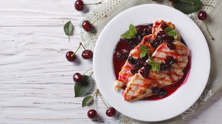 A plate of grilled chicken with a cherry sauce and green garnishes