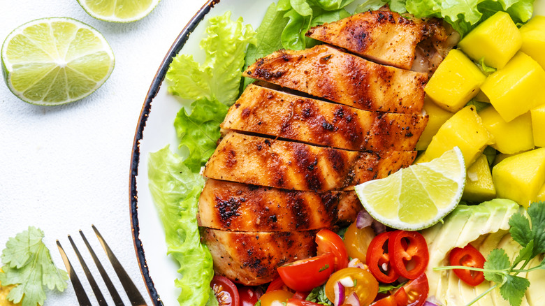 A grilled chicken breast in a salad with mango, avocado, and lime