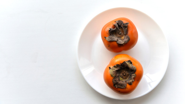 Two whole persimmons on a white plate and white background