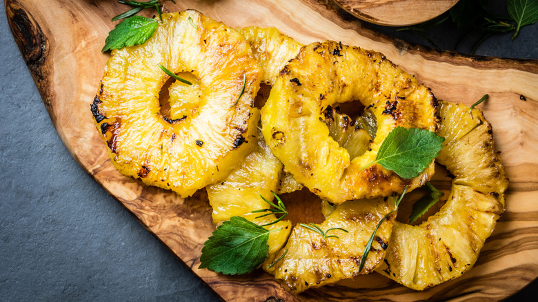 Grilled pineapple wheels garnished with mint leaves arranged on a wooden board