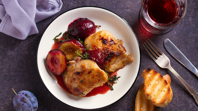 Chicken thighs and cooked plums in sauce with thyme sprigs as garnish