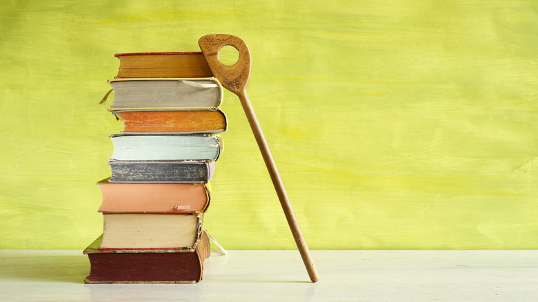A stack of vintage cookbooks, with a sauce spoon leaning on them