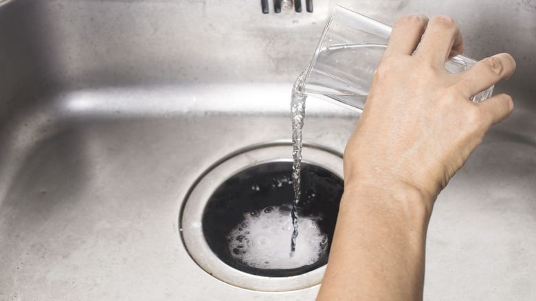 Hand pours vinegar over baking soda in sink drain