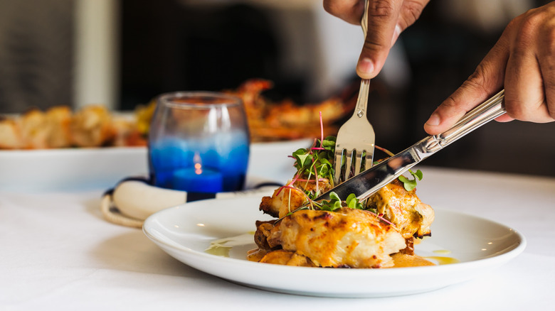 Hands cutting into plated dish with fork and knife