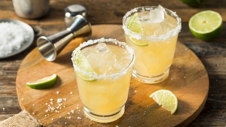 Two margaritas on a wood board with limes