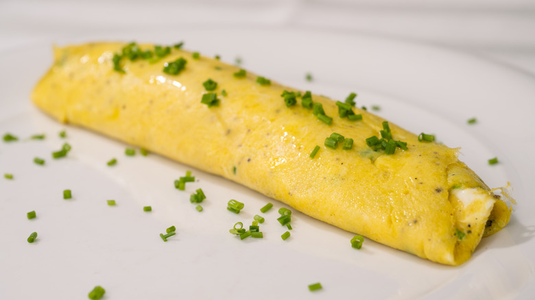A French-style omelet garnished with diced chives on a white plate