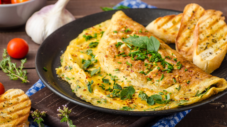 An omelet garnished with herbs and chili flakes and a side of toast, on a black plate