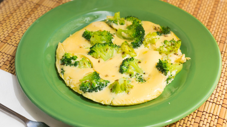 A flat omelet with broccoli florets sticking out on a green plate