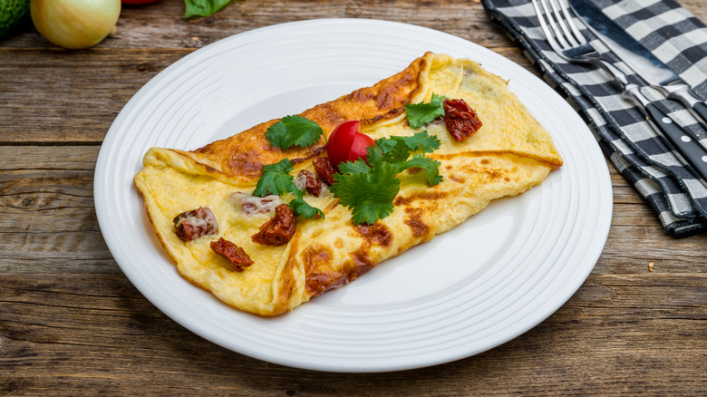 An omelet with sun dried tomatoes and parsley semi-folded on a white plate