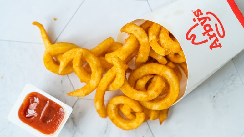A box of Arby's curly fries next to an open container of ketchup.