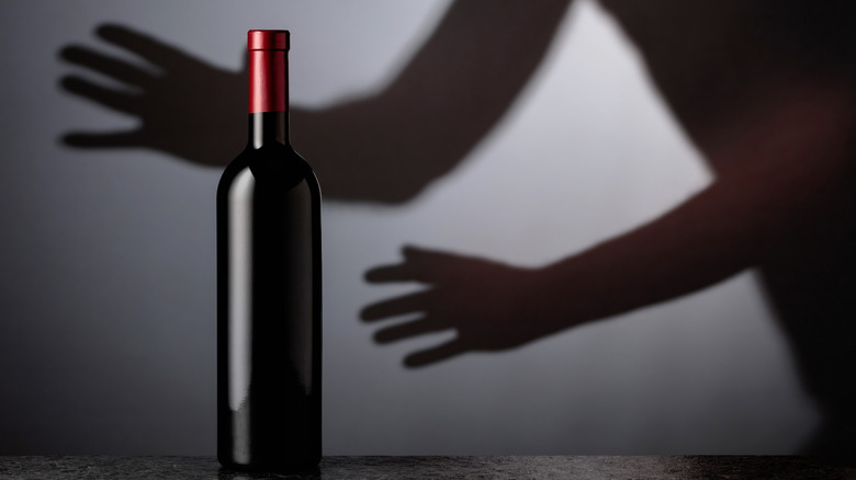 Shadows on a gray wall of hands reaching for a red wine bottle