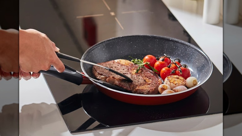Red and black non-stick frying pan with steak and vegetables on a stovetop
