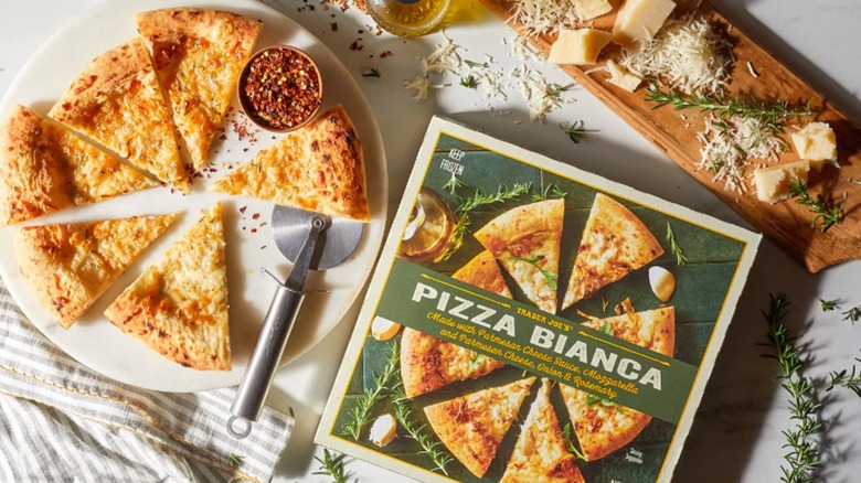 Trader Joe's Pizza Bianca with grgeen box and pizza on plate with parmesan and rosemary sprigs on the table.