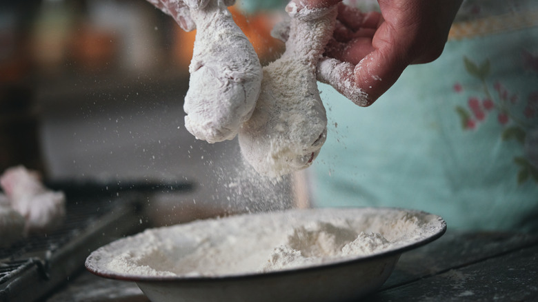 Dredging raw chicken drumsticks in flour.