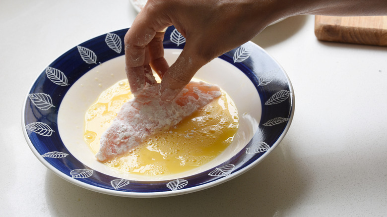 Hand dipping chicken cutlet into egg wash.