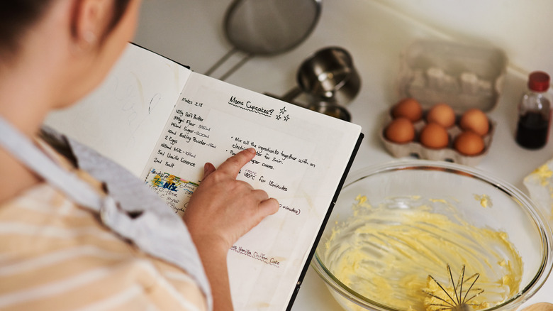 Person reading a recipe from a notebook over a counter with cooking items