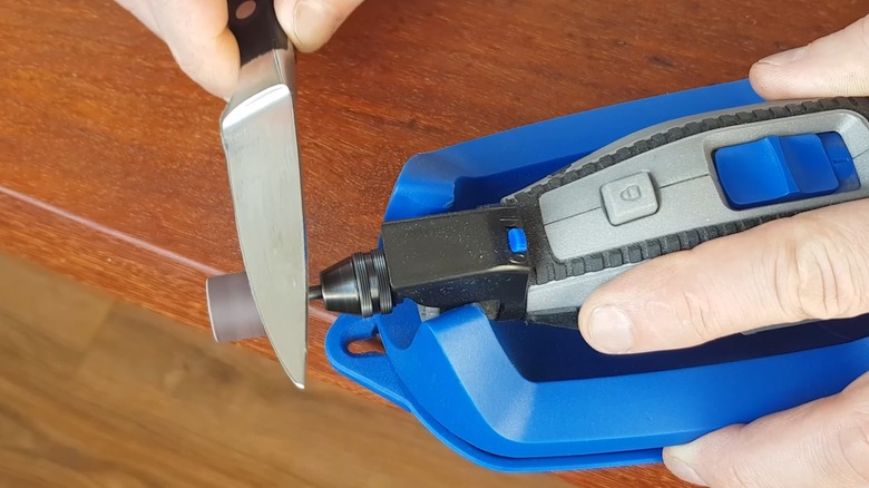 Male hands using a dremel-style rotary grinder to sharpen a knife
