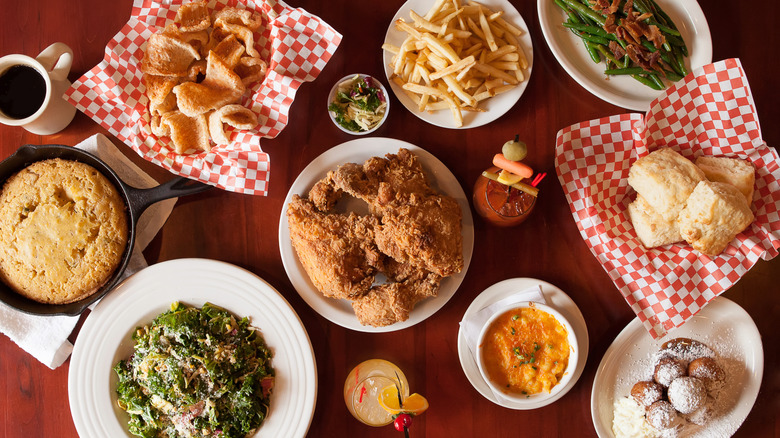 A table full of Southern comfort food including fried chicken, collard greens, skillet cornbread, and biscuits
