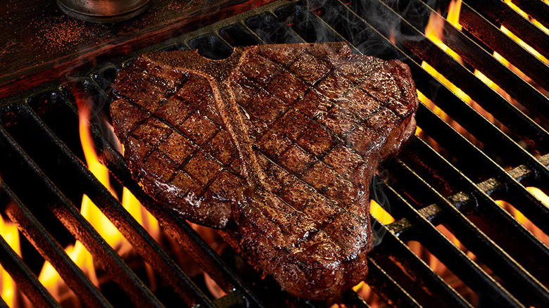 a porterhouse steak cooking on a fiery grill