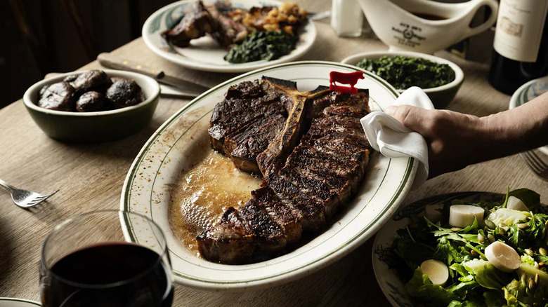 a porterhouse steak plated and sliced and served in the center of a table with other sides