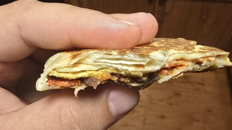 Hand holding a tiny crunchwrap with very little filling