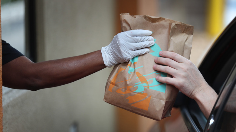 Gloved hand giving Taco Bell bag to customer in car