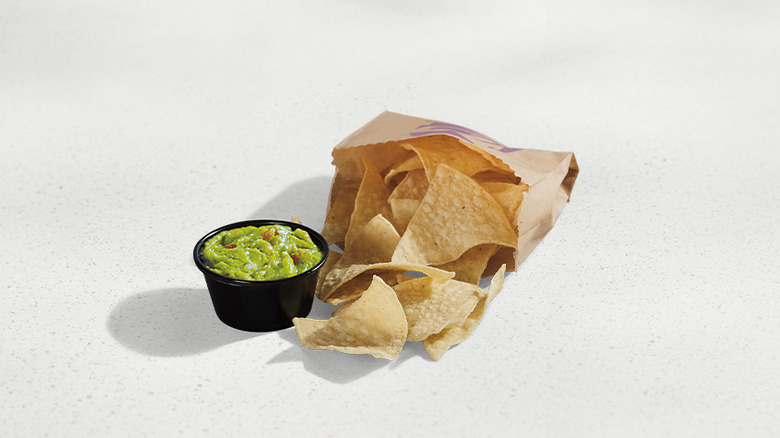 Taco Bell guacamole in a black cup and tortilla chips