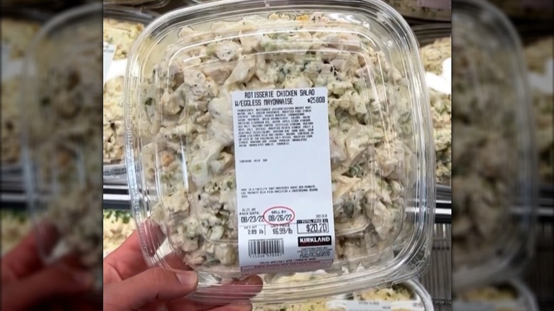 A hand holds a large container of rotisserie chicken salad from Costco