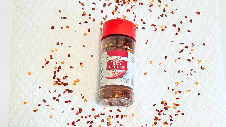 A bottle of Stonemill Crushed Red Pepper surrounded by crushed red pepper on a white background