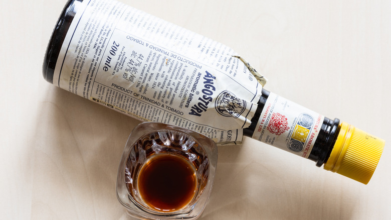 A bottle of Angostura bitters next to a shot glass with dark liquid inside