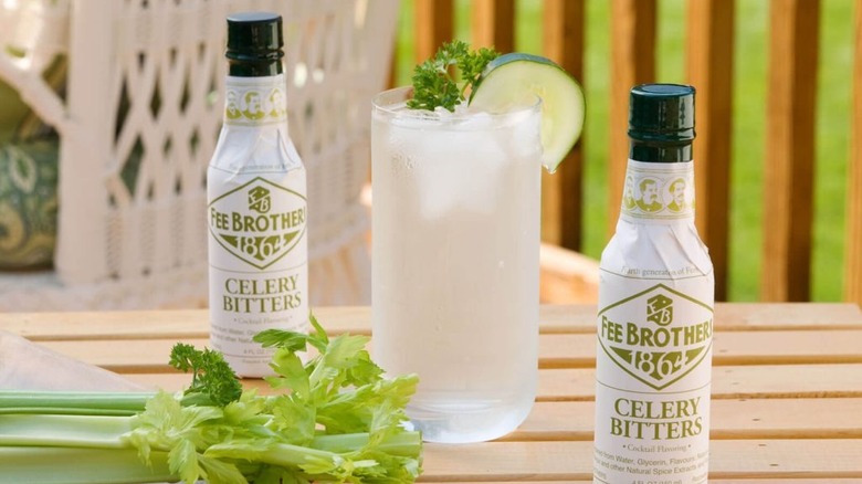 Two bottles of Fee Brothers celery bitters next to a clear cocktail and a stalk of celery on an outdoor table