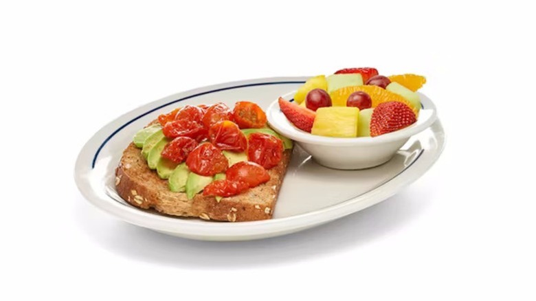 a slice of avocado toast with cherry tomatoes and a side cup of fresh fruit