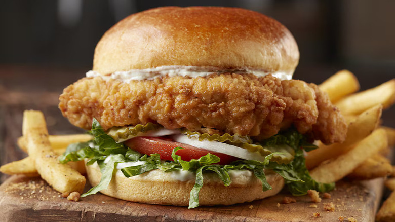 a thick-cut fried chicken breast sandwich with brioche bun, lettuce, tomato, onion, pickle, and mayo and a side of fries