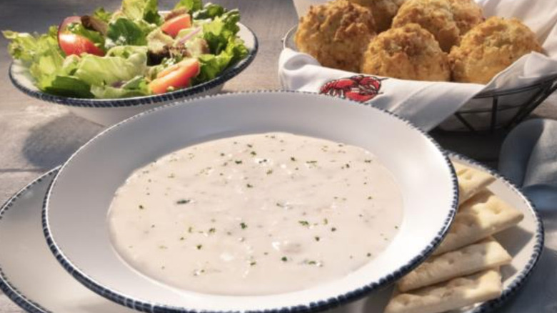 a bowl of New England clam chowder, a bowl of house salad, and a basket of Cheddar Bay biscuits on a table