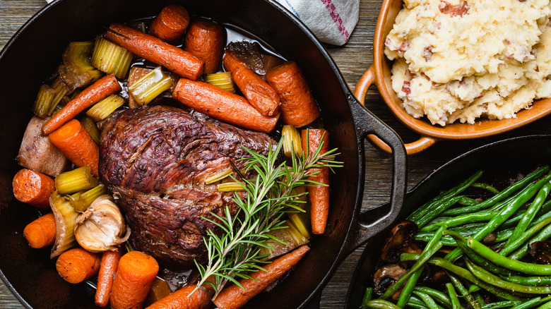 A top view of a pot roast in a cast iron Dutch oven with mashed potatoes and green beans on the side